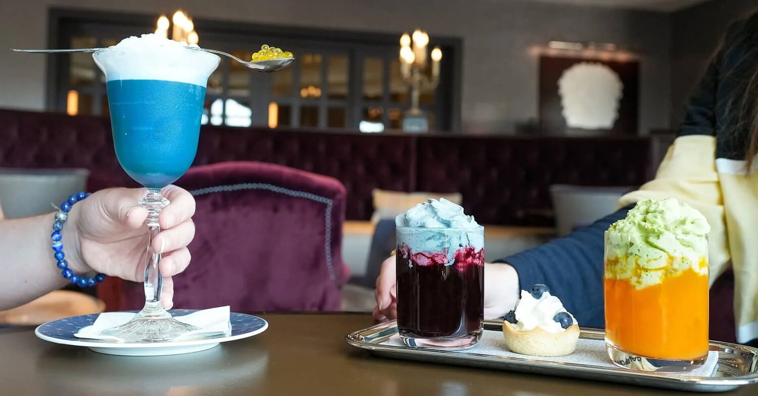 Getränke Princess Week Drei Getränke mit Sahnehauben auf einem Tisch, zudem ein kleines Küchlein mit Blaubeeren