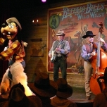 Goofy im Cowboyoutfit steht mit einer Country-Band auf der Bühne