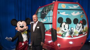 Mickey Mouse steht vor einer Gondel des Disney Skyliners