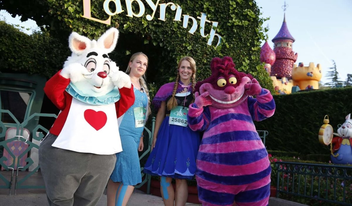 zwei junge Läuferinnen zusammen mit dem Weißen Kaninchen und der Grinsekatze vor dem Labyrinth im Fantasyland