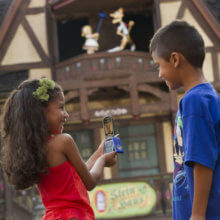 Zwei Kinder stehen mit Mobiltelefon vor einem Pavillion und spielen Disney's Phineas and Ferb: Agent P´s World Showcase Adventure