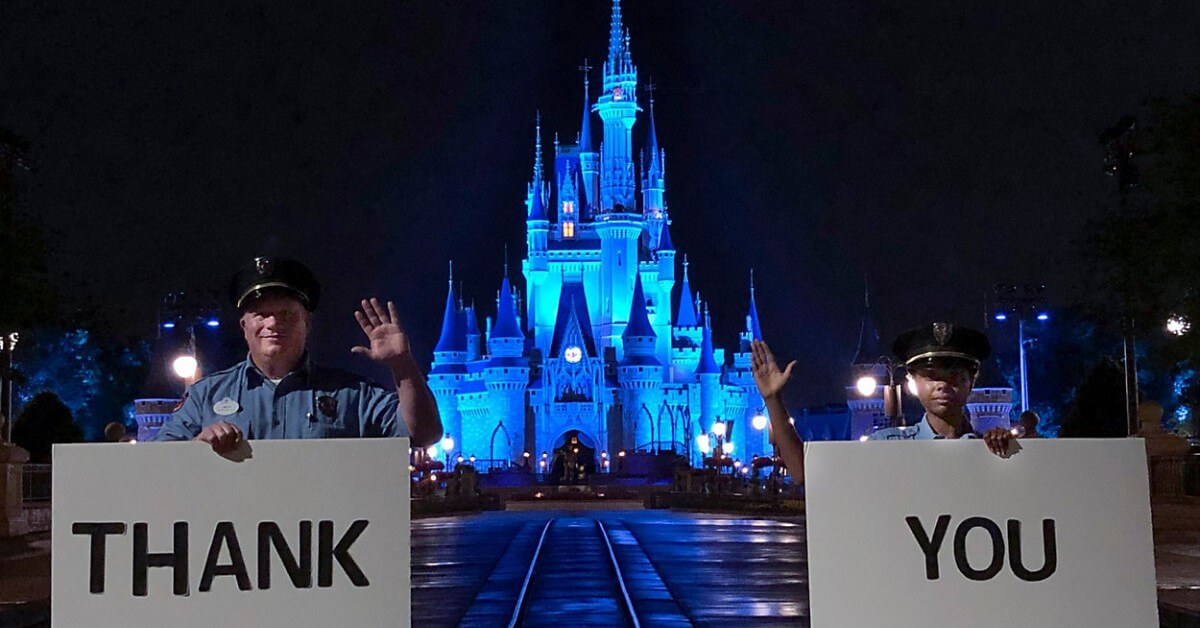 Blau erleuchtetes Cinderella Castle als Dank für Hilfskräfte - zwei Cast Member halt Tafeln mit der Aufschrift Than you