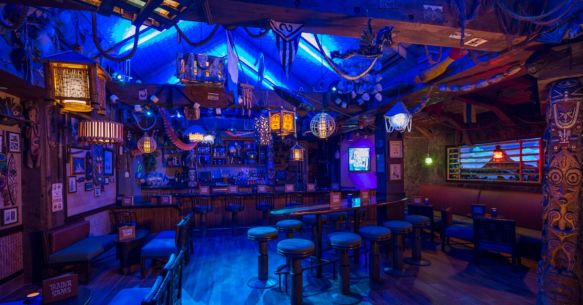 Stimmungsvoll beleuchteter Gastraum von Trader Sam's Tiki Bar. Dekogegenstände und Lampen hängen von der Decke, vor dem Fenster ist ein Vulkan zu sehen