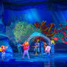 Auf der Bühne der Musicalshow Finding Nemo - The Musical stehen mehrere Darsteller mit großen Puppen in Form verschiedener Fische