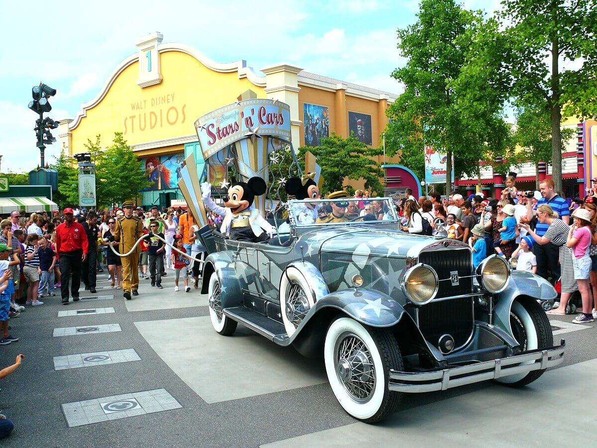 Inmitten einer Menschenmenge ist in den Walt Disney Studios ein Auto der Disney's Stars and Cars Parade mit Mickey und Minnie Mouse zu sehen