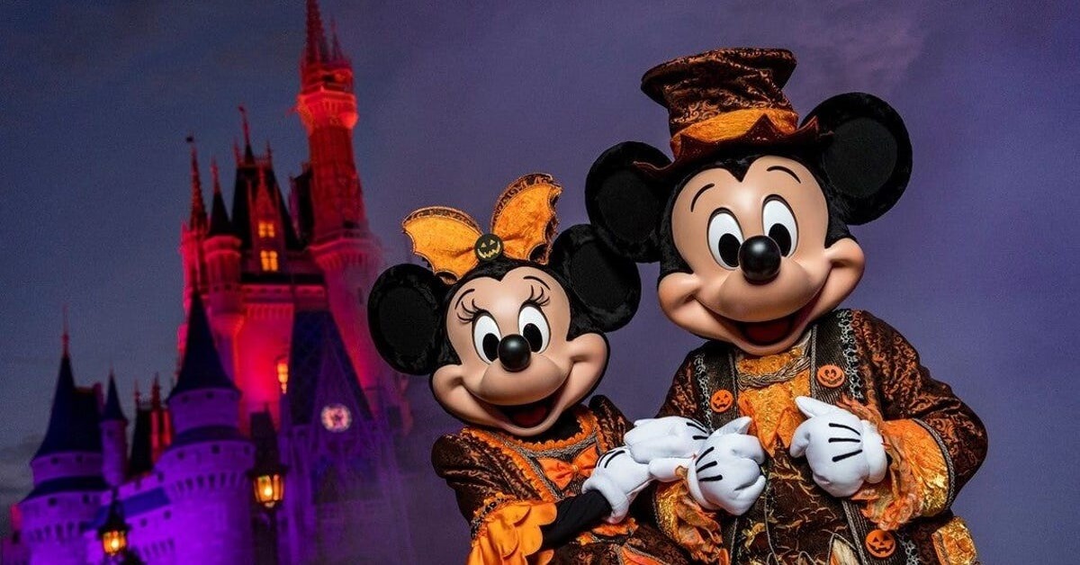 Mickey und Minnie stehen in orange-schwarzen Halloweenkostümen vor dem Cinderella Castle im Magic Kingdom