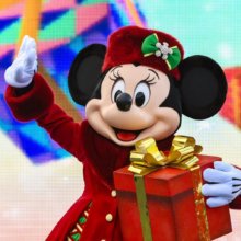 Minnie Mouse mit weihnachtlichem Outfit winkt und hält ein Geschenk im Arm