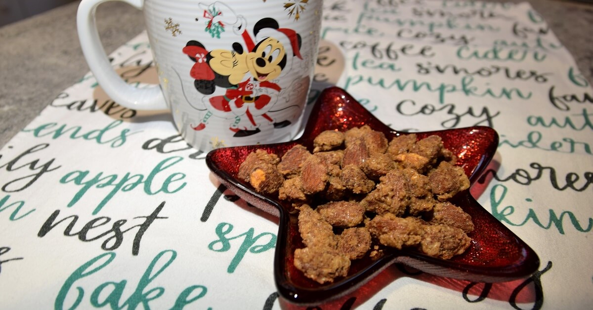 Die fertig zubereiteten Glazed Almonds nach Disney World Rezept liegen in einer sternförmigen Schale neben der eine Tasse mit weihnachtlichem Disneymotiv zu sehen ist