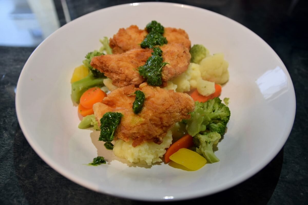 Auf einem großen Teller ist eine Portion des Fried Endorian Tip Yips mit Kartoffelstampf, Gemüse und Kräutersoße angerichtet