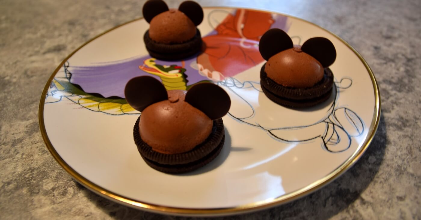 Auf einem Teller mit Fantasia-Motiv liegen drei Mickey Mousse Domes nach einem Rezept aus dem Chef Mickey's in Walt Disney World