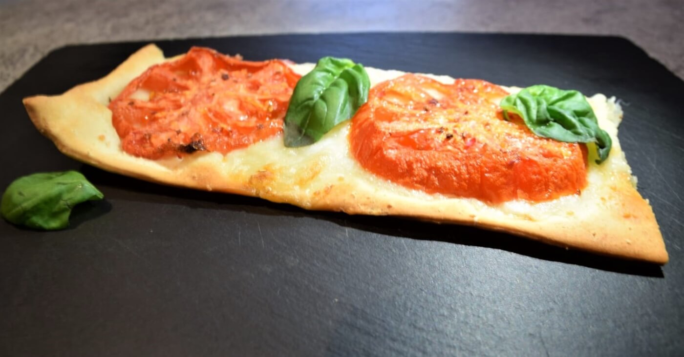 Auf einer Schieferplatte liegt ein Stück Tomaten-Flatbread mit frischem Basilikum