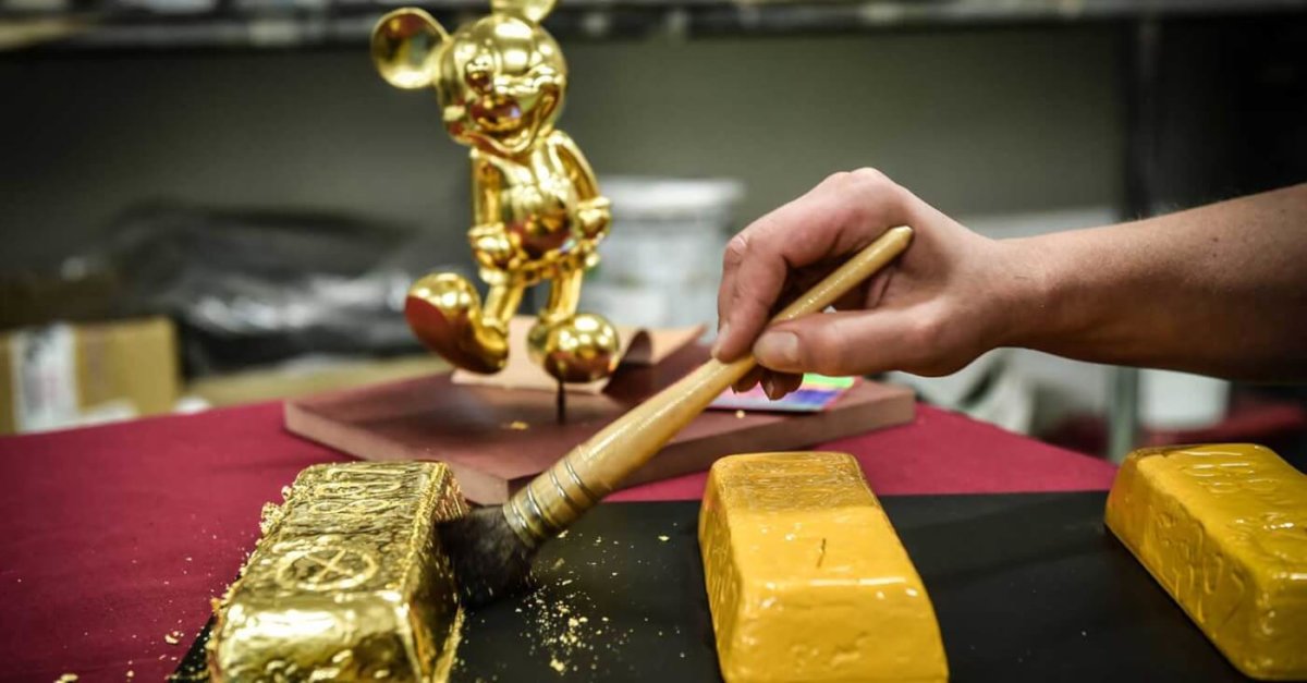 Pinsel vergoldet einen Gipsbarren, im Hintergrund eine goldene Mickey Statue