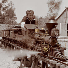 Walt Disney sitzt inmitten seiner aufgebauten Modelleisenbahn.