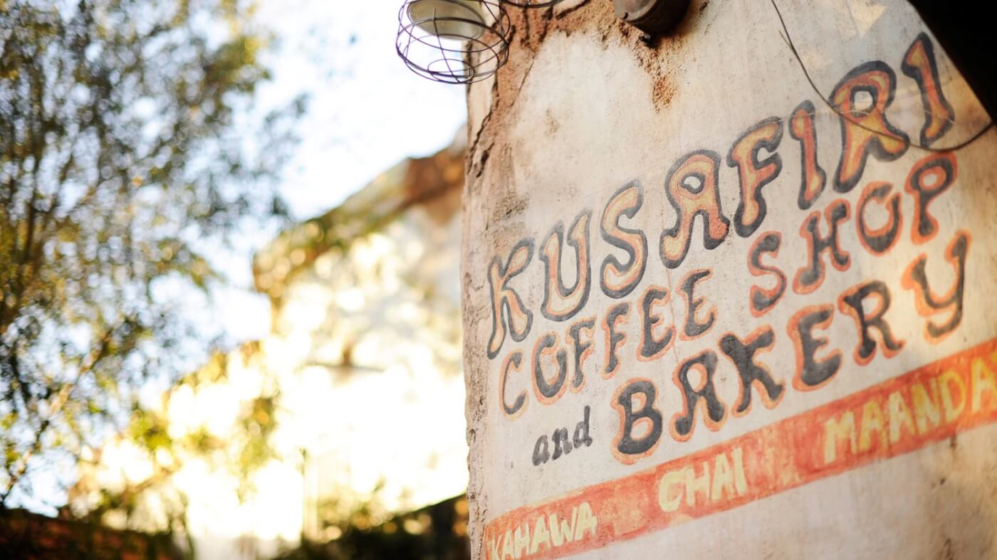 Eine Nahaufnahme der Fassade des Kusafiri Coffee Shop in Disneys Animal Kingdom zeigt den Schriftzug Kusafiri Coffee Shop and Bakery in bunten Lettern