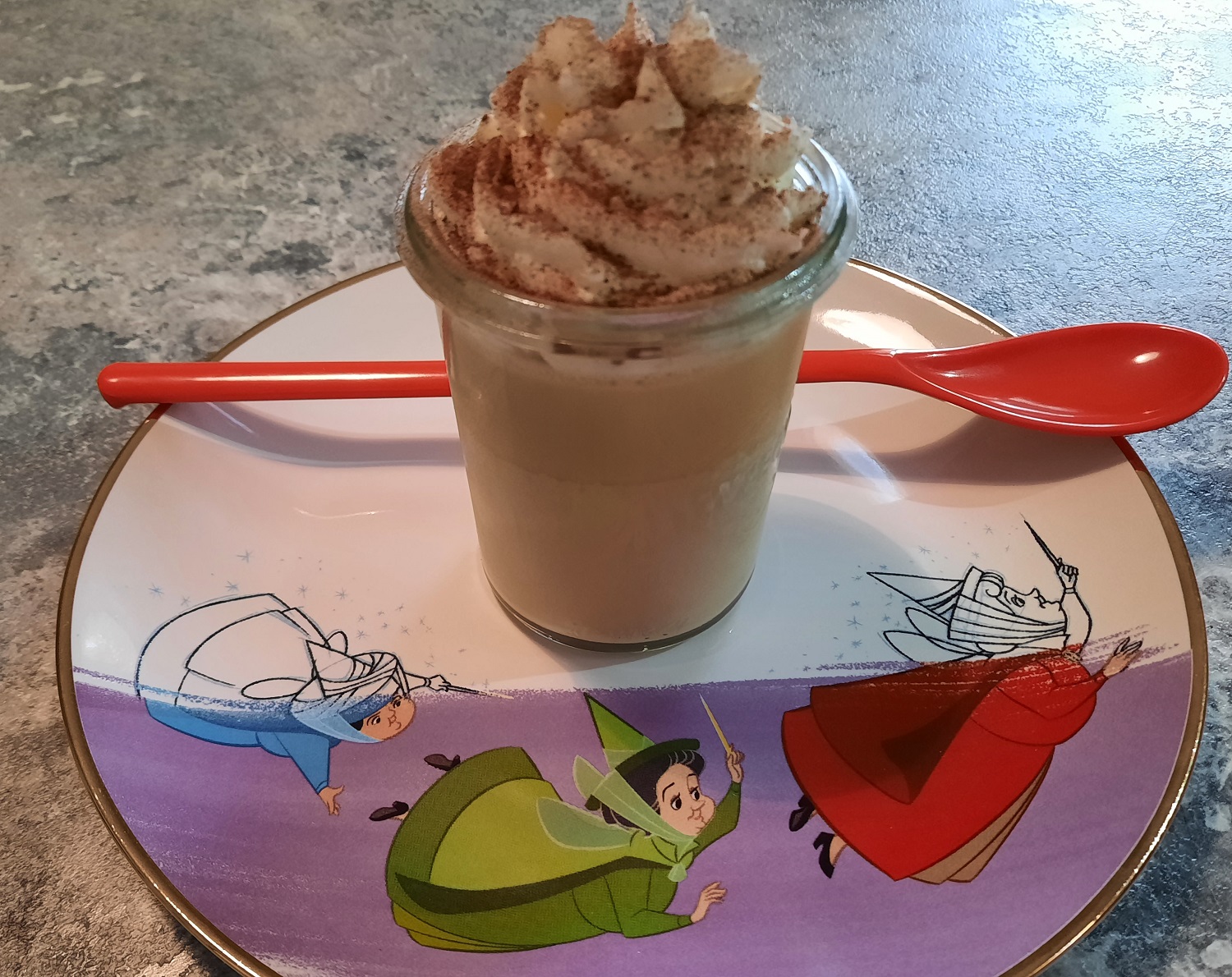 Nachtisch in einem Dessertglas mit langem rotem Löffel auf einem Dessertteller mit Disney Motiv