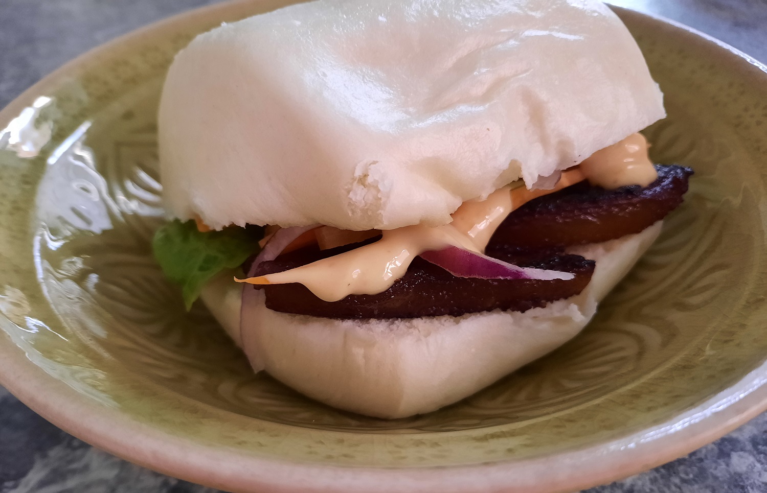 Ein asiatisches Burgerbrötchen mit Schweinebauch, Sriracha-Mayonnaise, Salat, Zwiebeln und Karottenstreifen