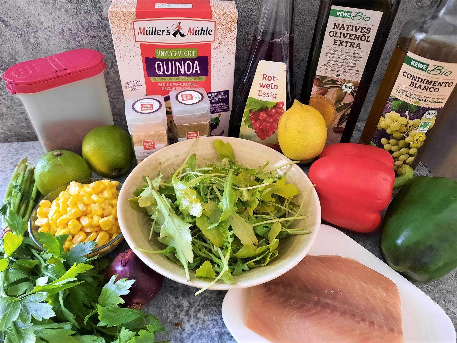 Verschiedene frische Zutaten wie Rucola, Paprika oder Limetten mit einem Lachsfilet und mehreren anderen Zutaten