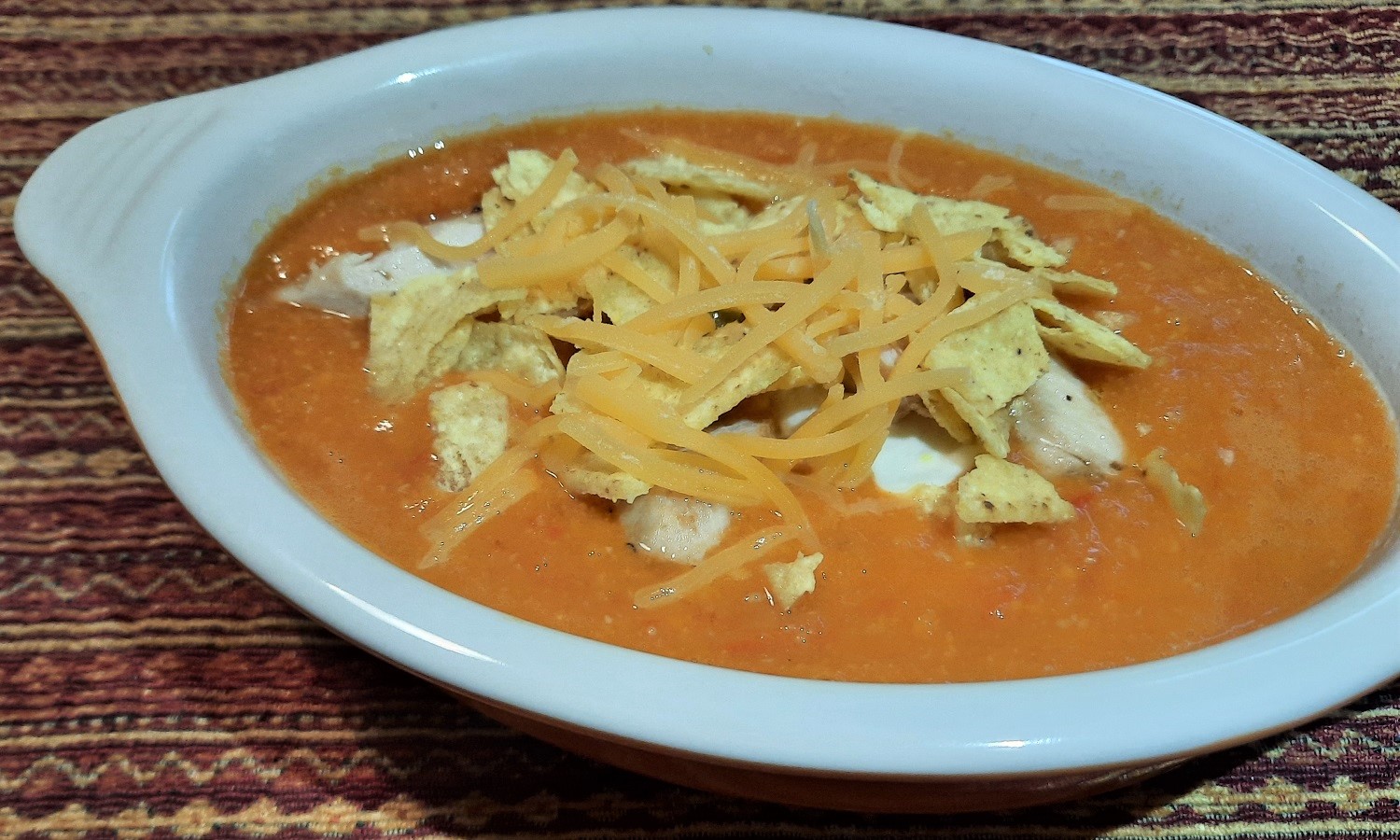 Suppe garniert mit Tortilla Chips, Hähnchenstreifen und Cheddar