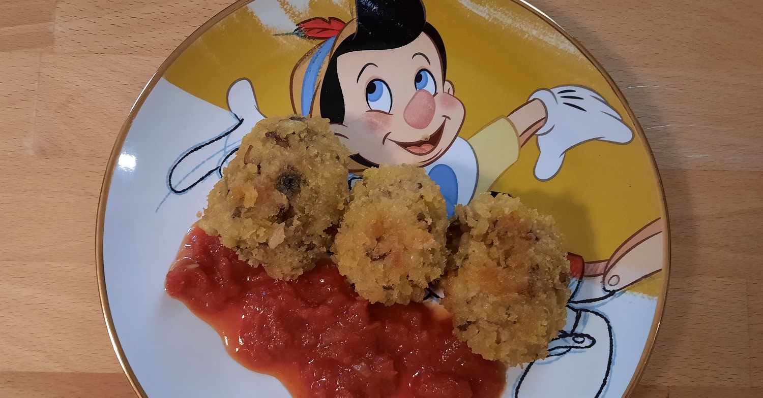 Drei frittierte Risottobällchen sind mit Tomatensauce auf einem Teller mit Pinocchio-Motiv angerichtet