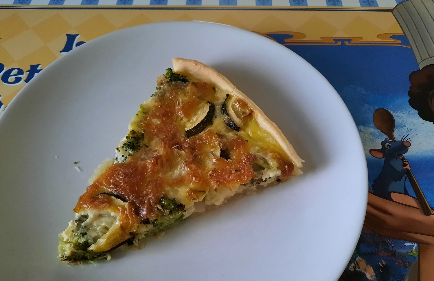 Ein Stück Gemüse-Quiche auf einem Platzset mit Ratatouille-Motiv