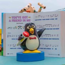 Toy Story Hotel - Pinguin Wheezy steht mit Mikro vor dem Song-Buch