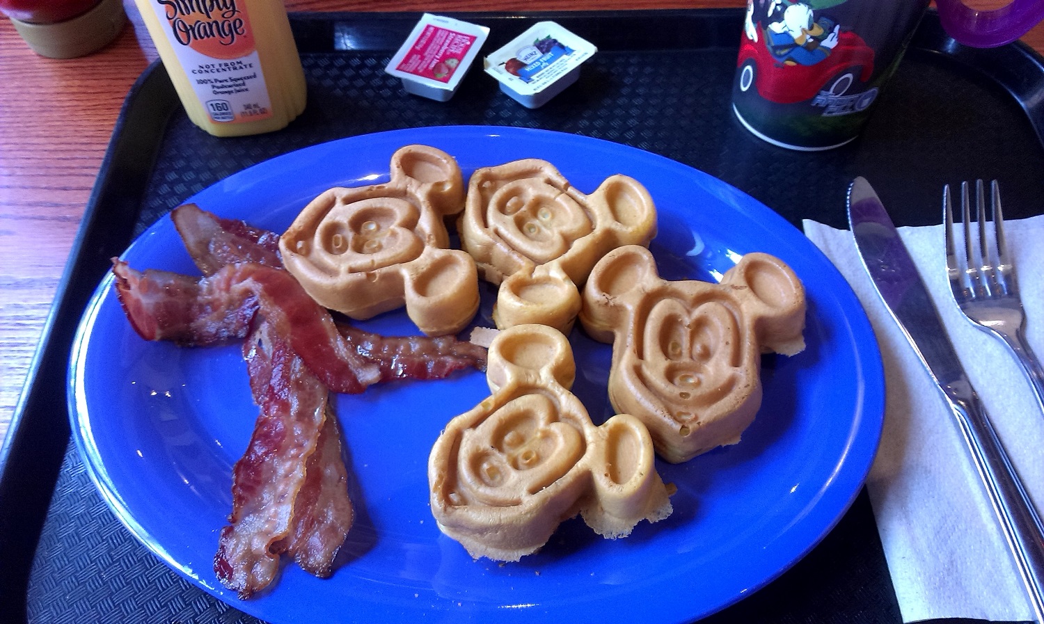 Vier Waffeln in Mickey Mouse Form und Speck auf einem blauen Teller