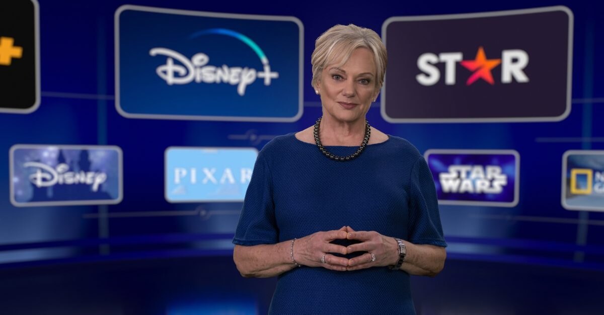 Christine McCarthy in einem dunkelblauen Kleid vor einem Bildschirm mit Disney Plus Einblendungen