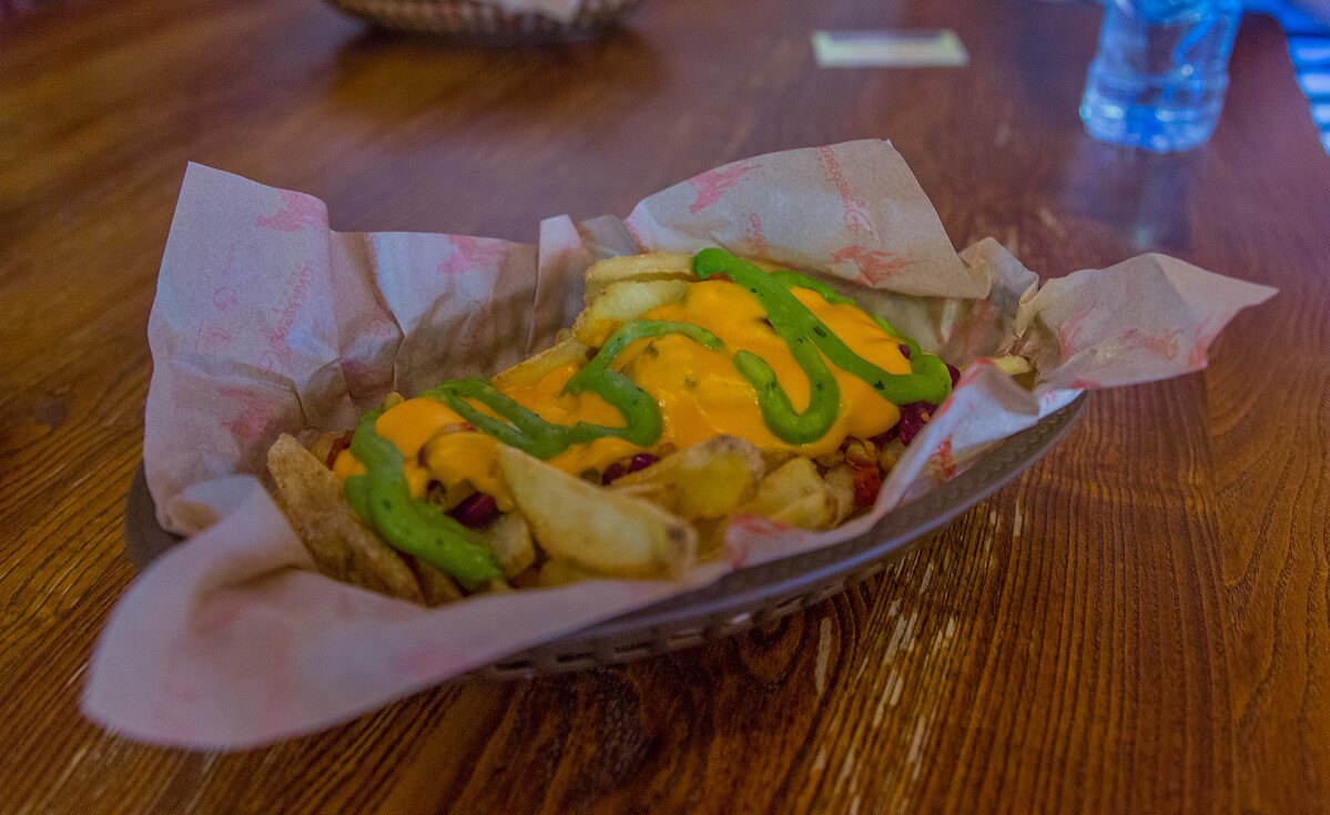 Pommes Frites mit einer Käsesauce und einer grünen Sauce, serviert in einem kleinen Plastikkorb, der mit Papier ausgelegt ist