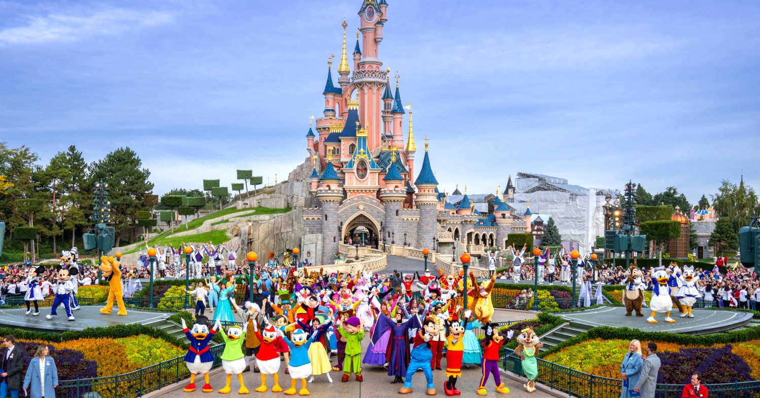 Gruppenfoto der Disney Figuren vor dem Sleeping Beauty Castle, rechts am Bildrand Natacha Rafalski