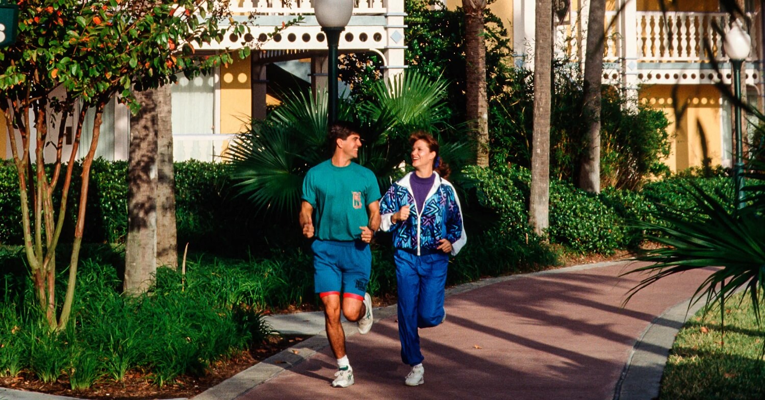 Zwei Personen in Sportkleidung joggen auf einem Pfad durch Disneys Caribbean Beach Resort