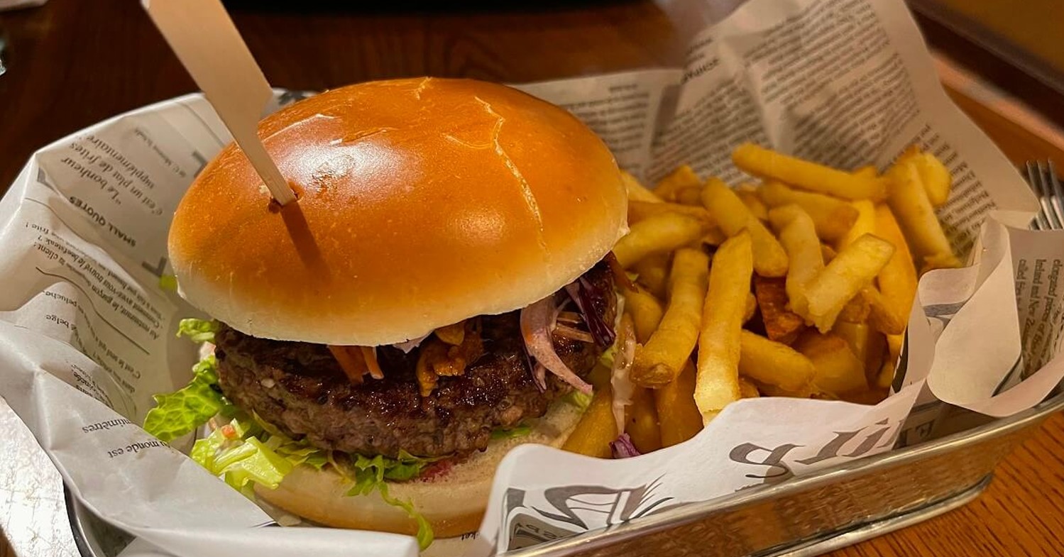 Ein Burger mit Pommer werden in einem Metallkorb, der mit Zeitungspapier ausgelegt ist, serviert