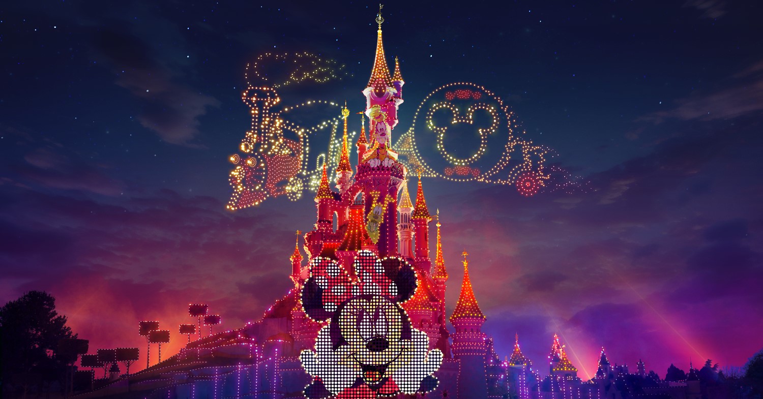 Disney Electrical Sky Parade mit einer Projektion von Minnie Mouse am Sleeping Beauty Castle und dem Zug der Main Street Electrical Parade, der in Form von Drohnen über die Himmel am Dornröschenschloss fährt