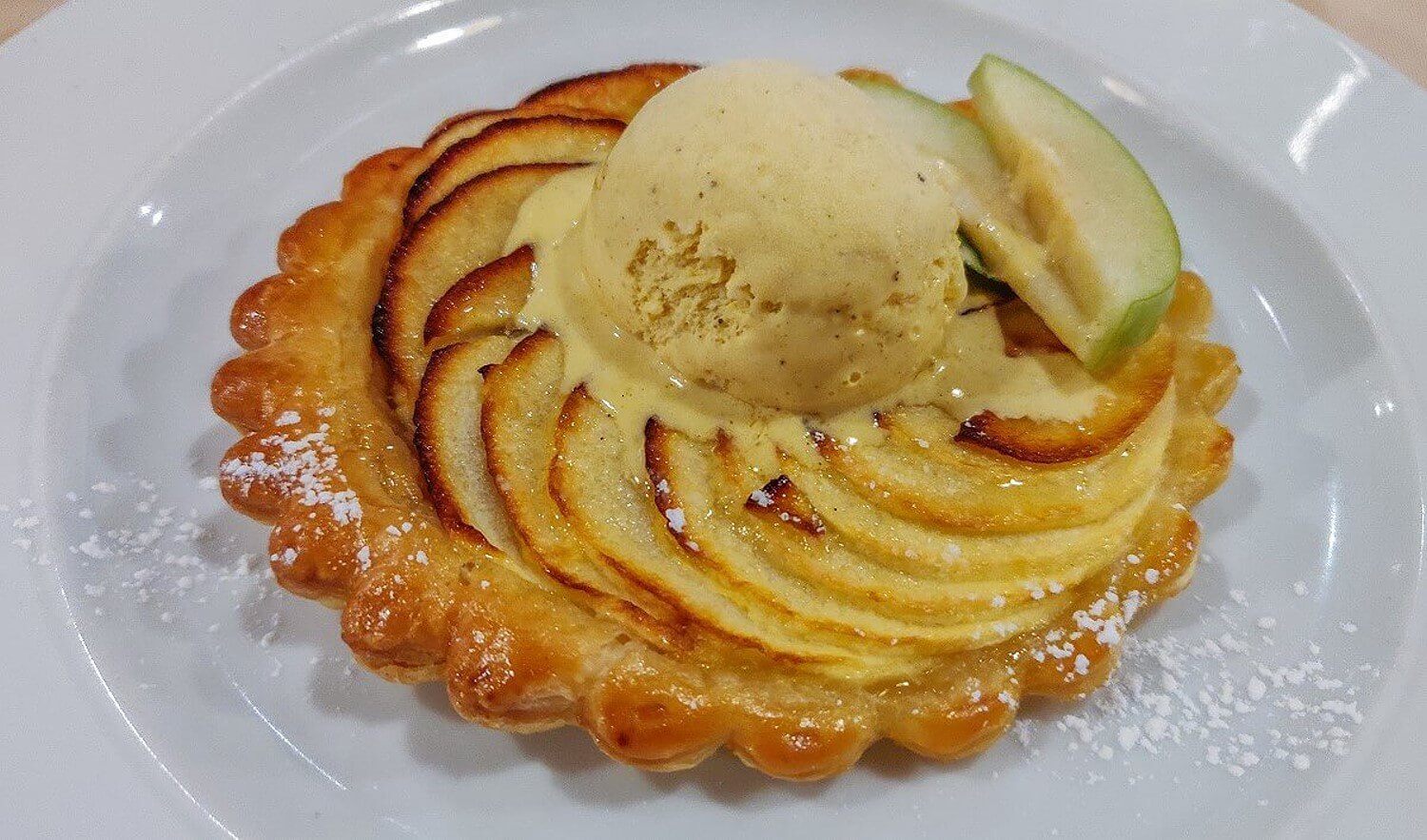 Tarte Tartin mit einer Kugel Vanilleeis, die langsam schmilzt und zwei frischen Apfelspalten