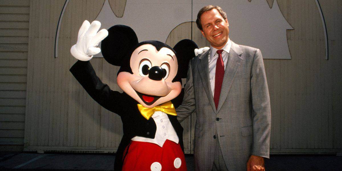 Mickey Mouse winkt, neben ihm steht der frühere Disney CEO Michael Eisner und lächelt