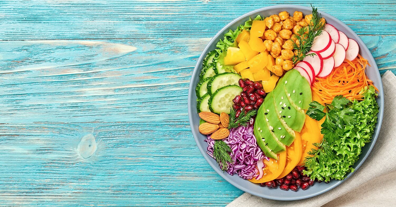 Ein Teller mit einem veganen Salat mit Avocado, Kichererbsen, Gurke, Radieschen, Mandeln, Granatapfeln und anderem Gemüse und Salaten