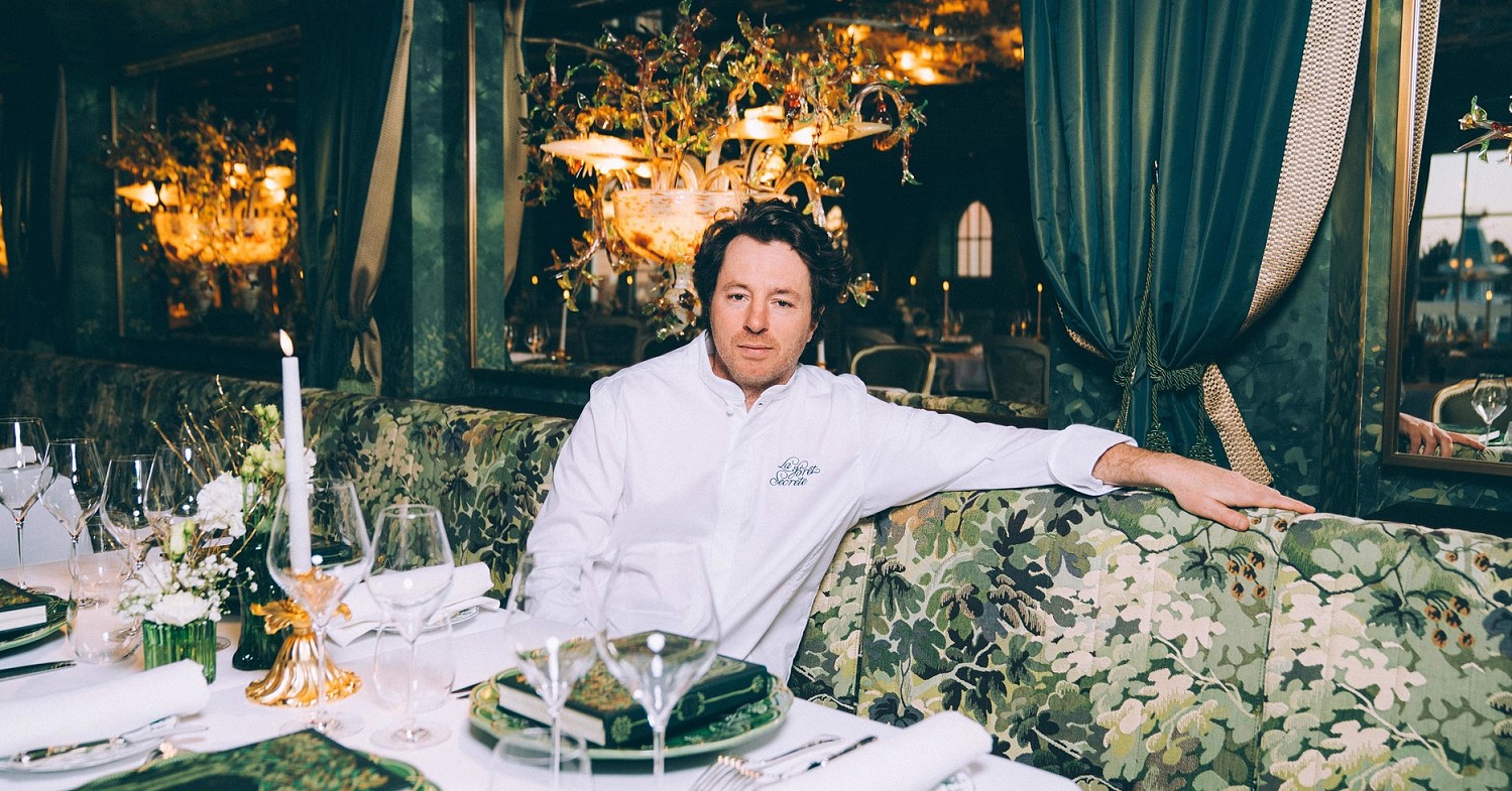 Jean Imbert in weißer Kochjacke sitzt auf einem Sofa im Restaurant La Foret Secrete