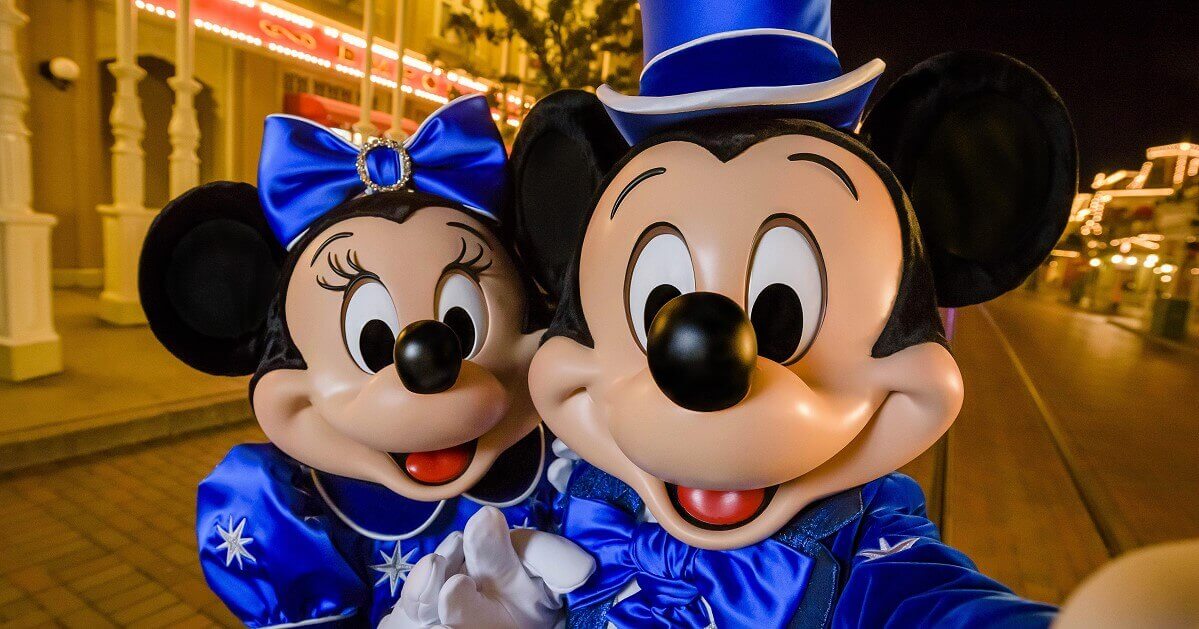 Mickey Mouse und Minnie Mouse machen ein Selfie auf der Main Street. Beide tragen Mitternachsblaube Kleidung mit silbernen Sternen